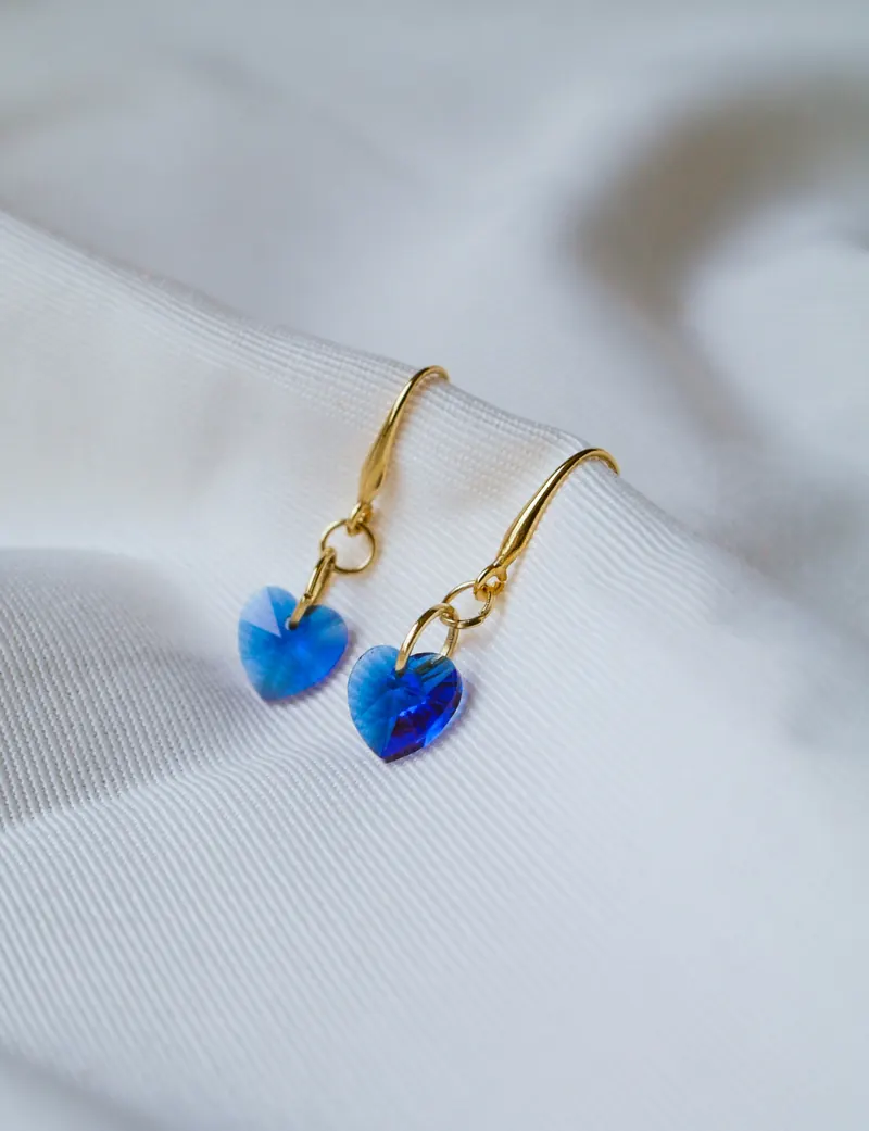 Blue crystal heart dangle earrings on gold hooks resting on white fabric