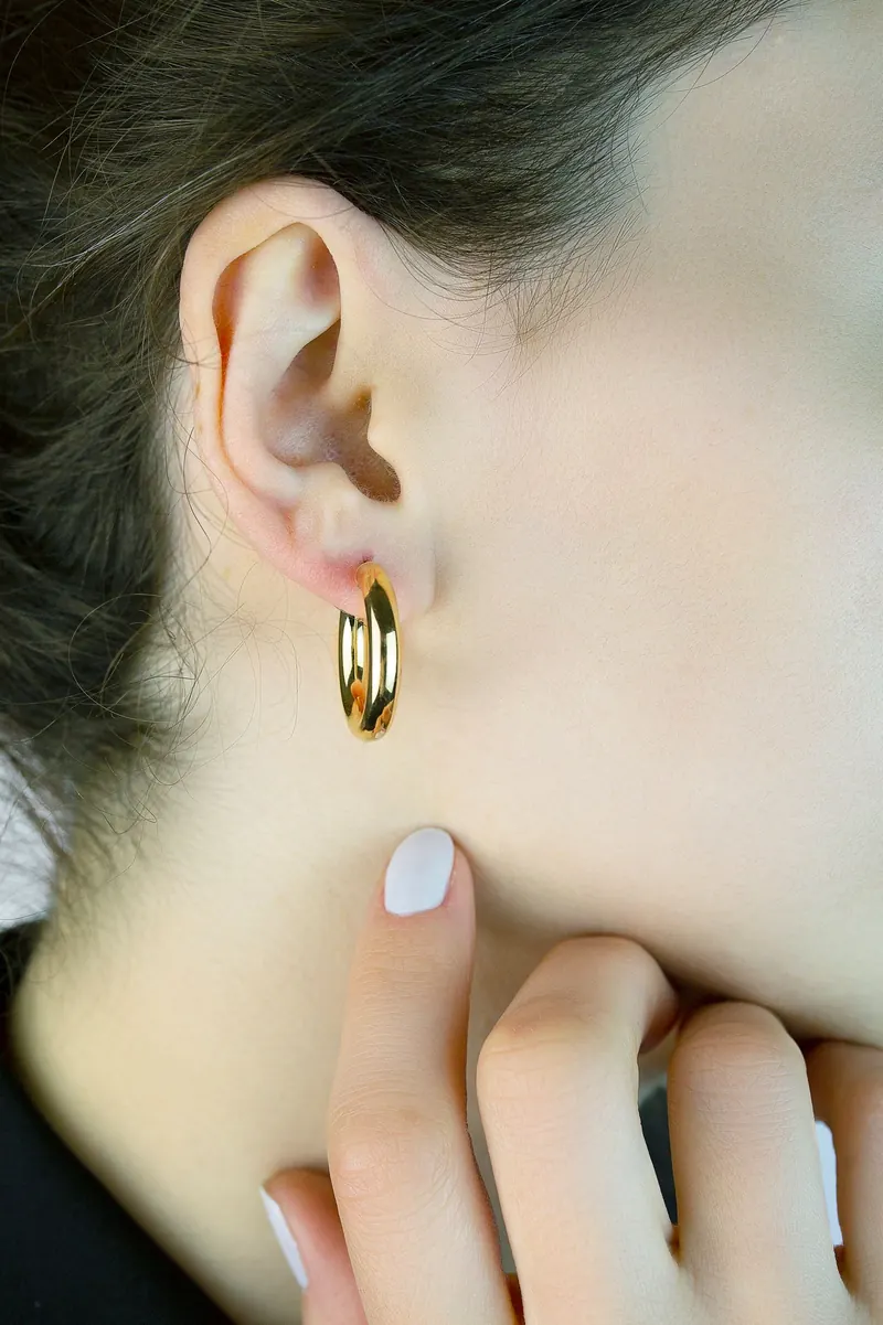 Close-up of a woman's ear with a small gold hoop, fingers touching her neck, the look self piercing earrings aim for