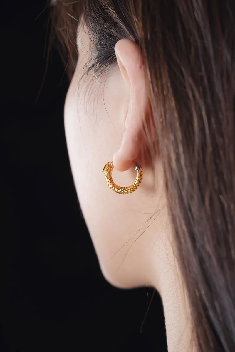 Profile of an ear with a textured gold huggie hoop against a black background, the kind of upper-ear look a triple forward helix piercing builds on