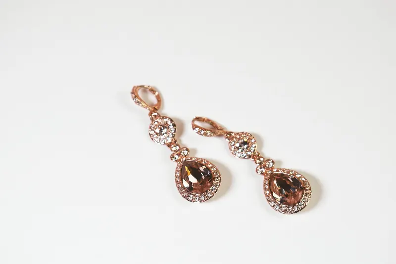 Rose-gold crystal pear drop earrings on a white background, a dangle style similar to the hanging half of behind the ear earrings