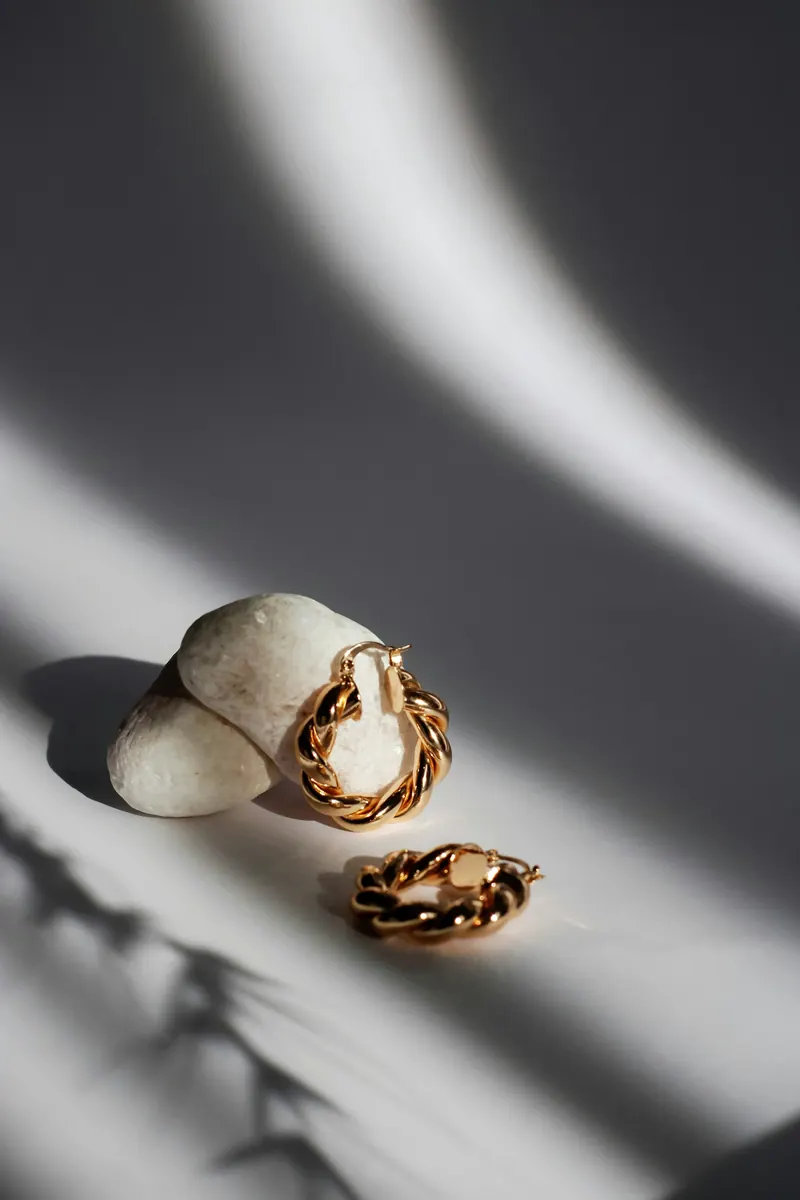 Twisted gold hoop earrings on white pebbles